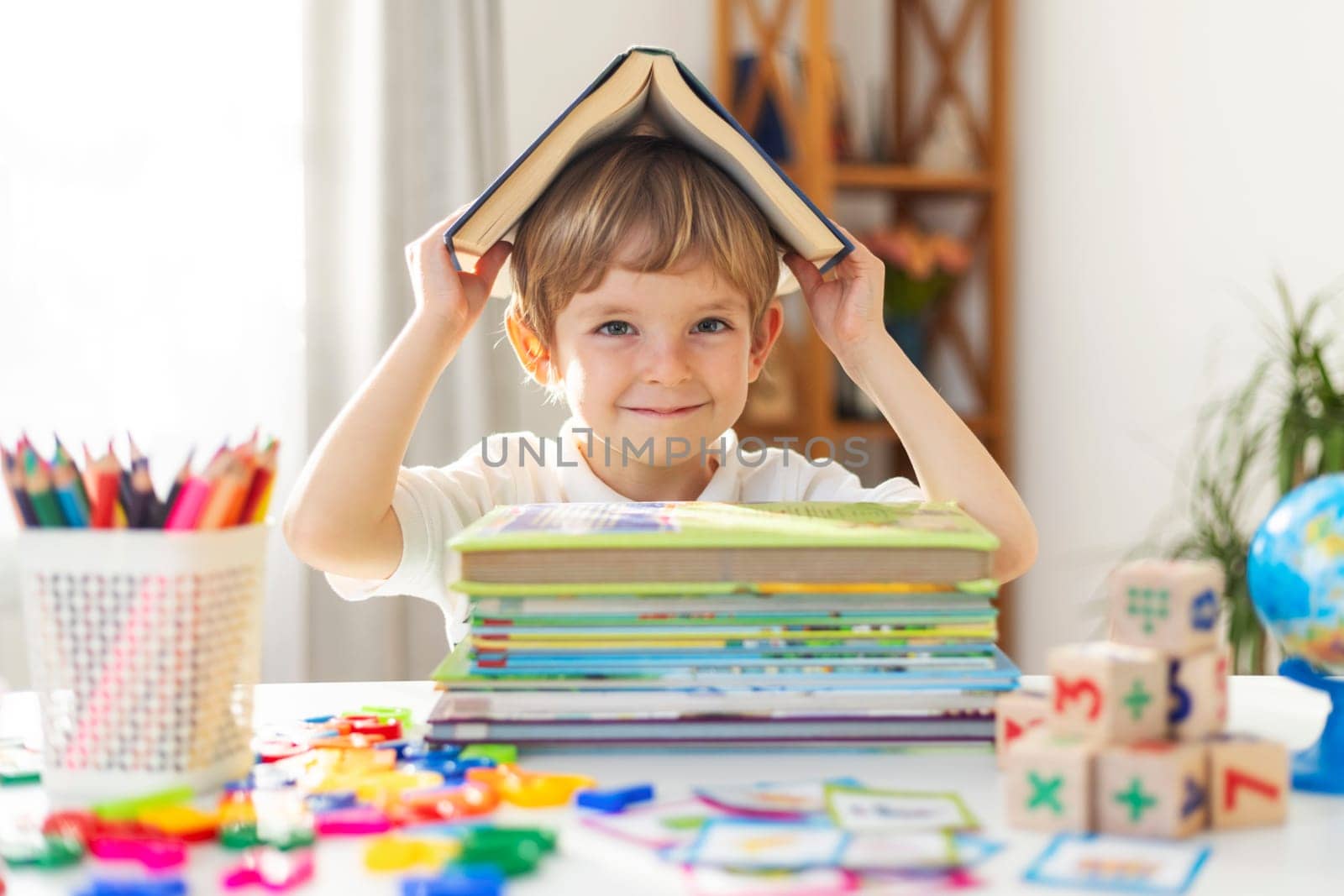 Boy with book on head at home learning space. Creativity and playful learning concept. Design for poster, educational material, banner.