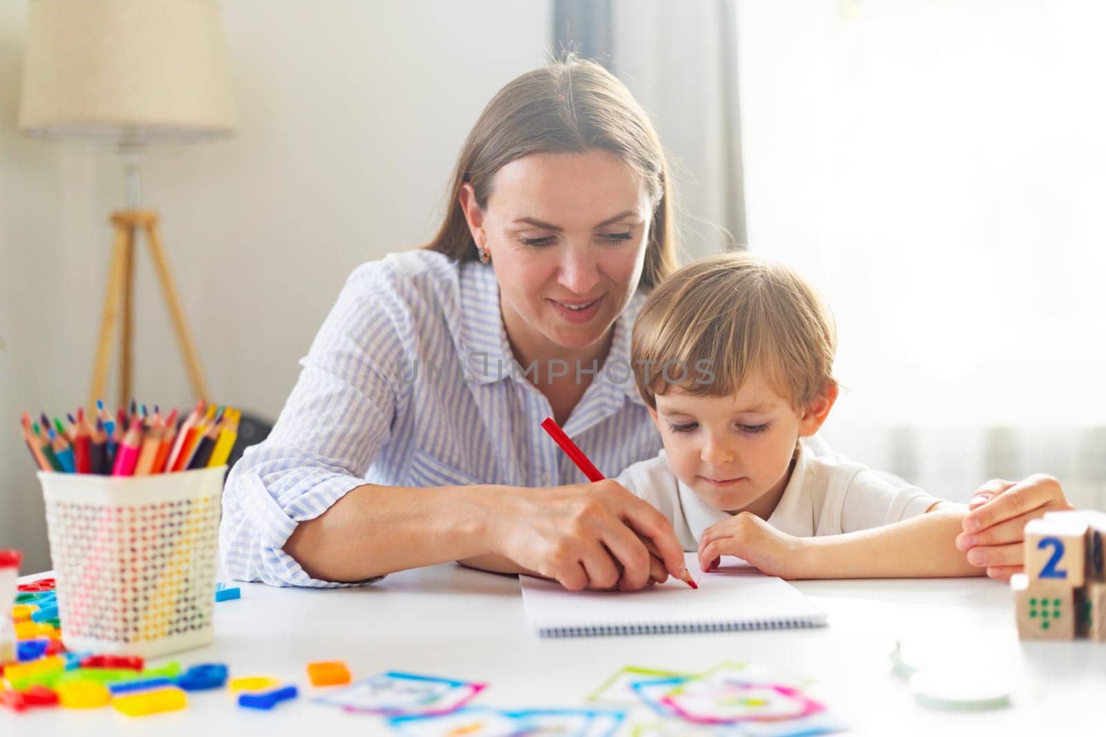 Woman and young boy drawing together, home learning concept. Indoor educational activity for design and greeting cards.