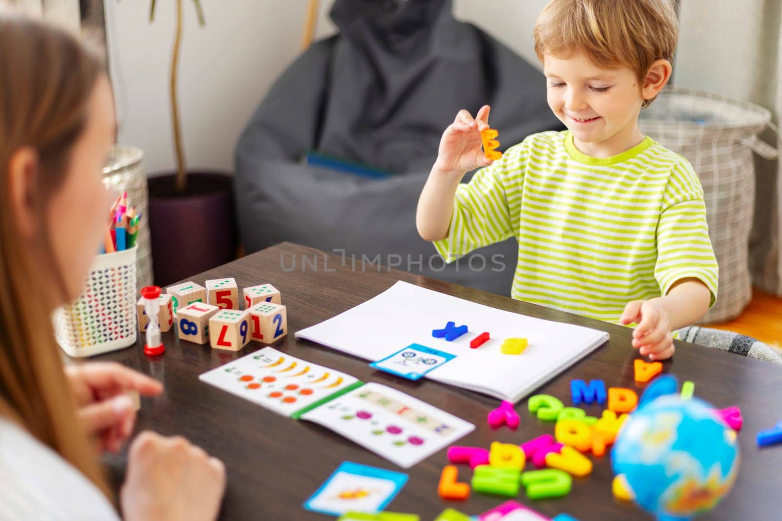 Young boy playing with letter block facing adult. Language development tools on table. Early education concept. Design for educational material