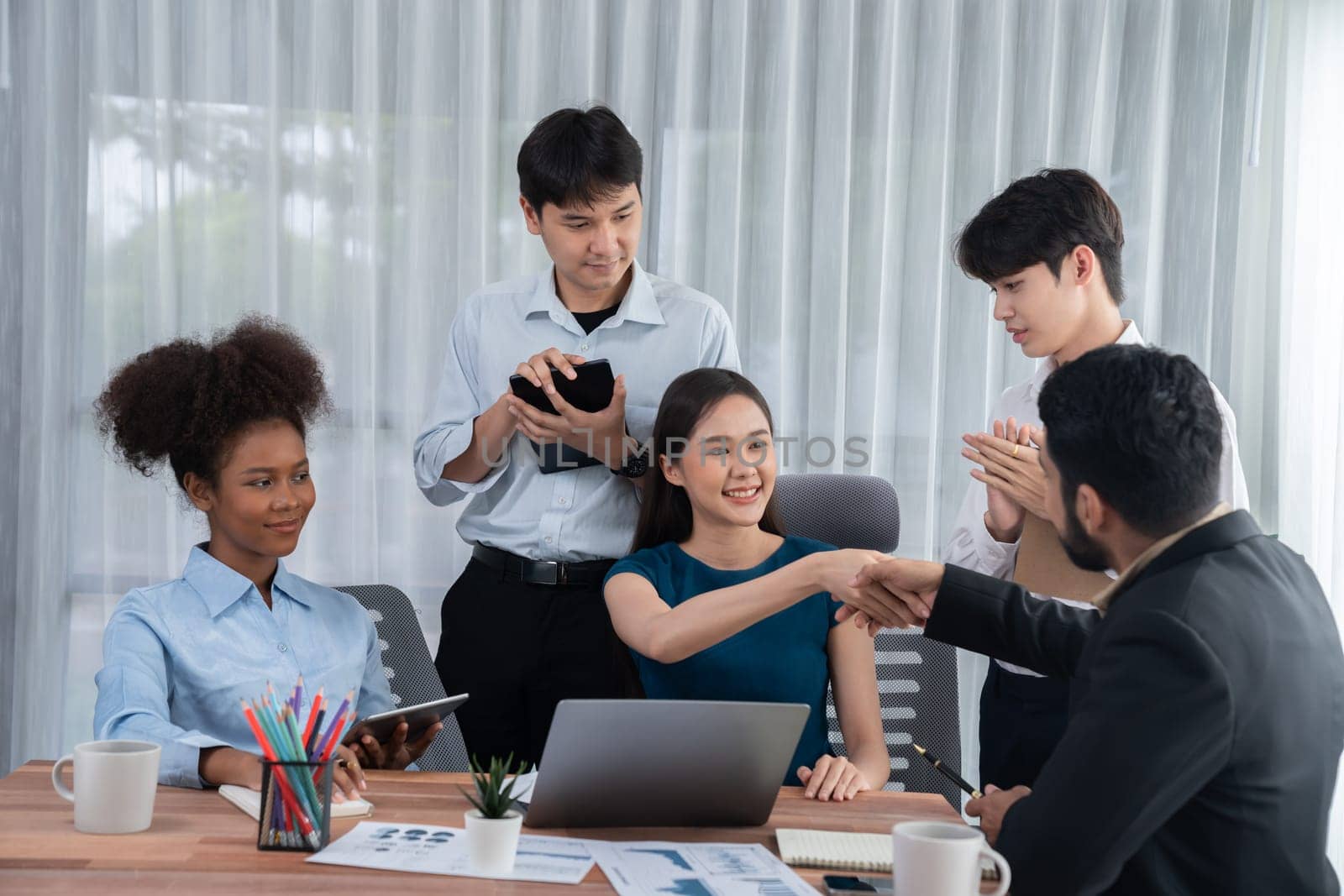 Diverse coworkers celebrate success with handshake and teamwork in corporate workplace. Multicultural team of happy professionals united in solidarity by handshaking in office. Concord