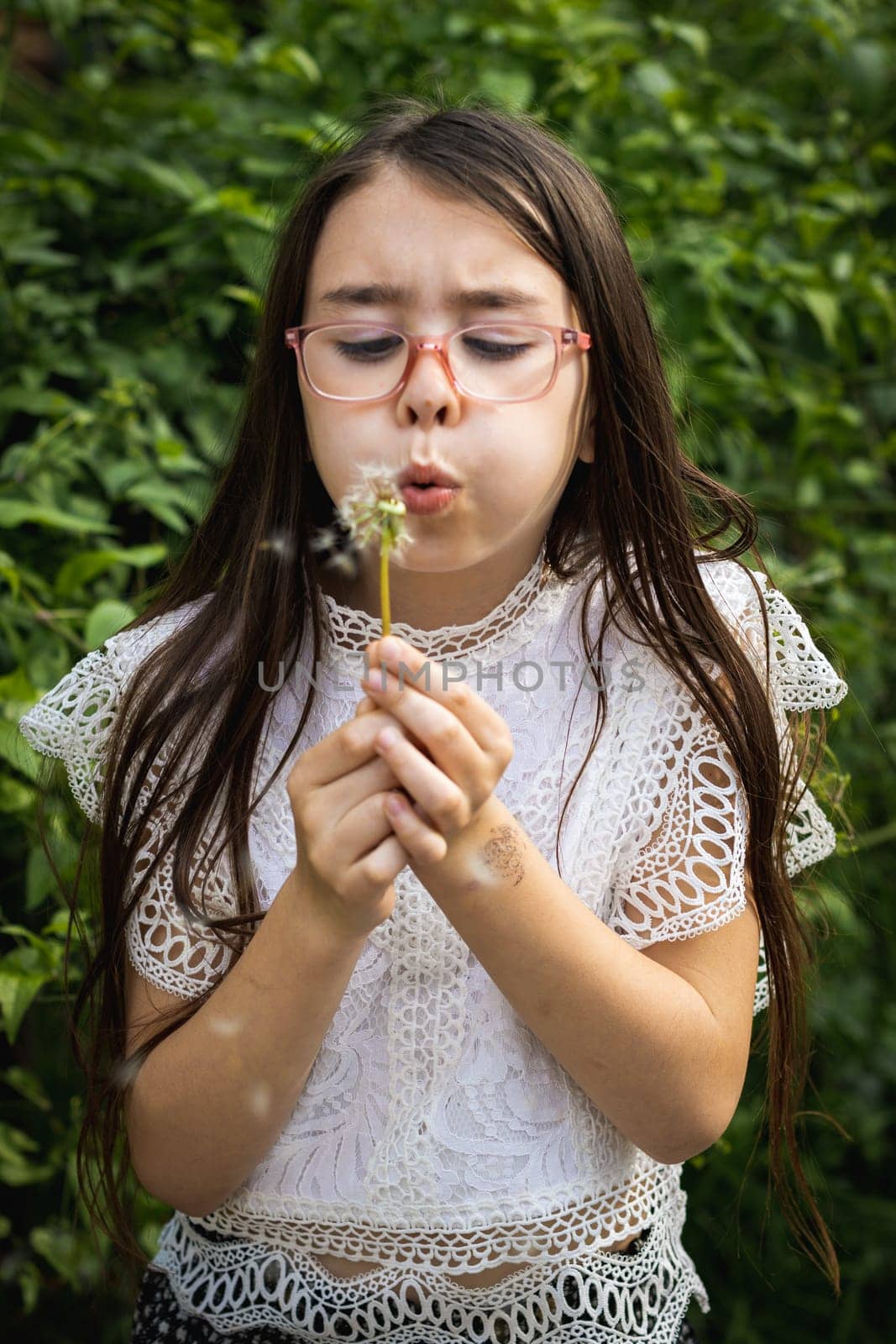 Portrait of a girl blowing a dandelion in the park. by Nataliya