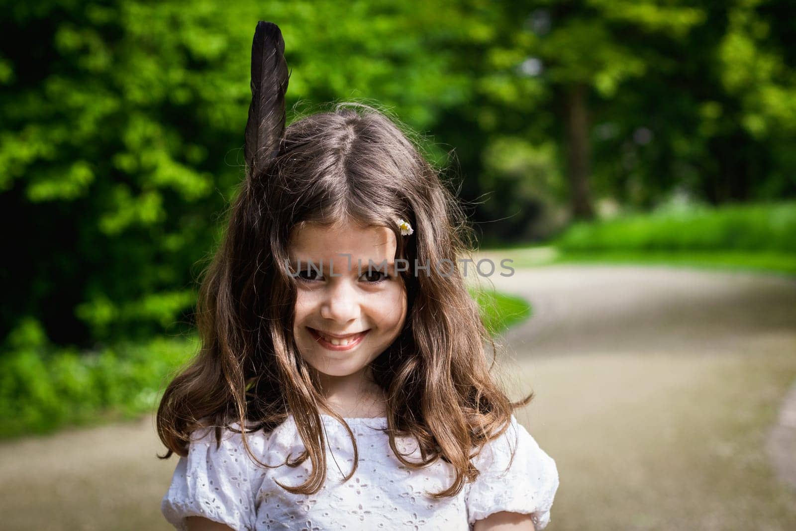 Portrait of one beautiful Caucasian happy smiling brunette girl with loose hair and black feather standing in the park on a spring day, close-up side view.