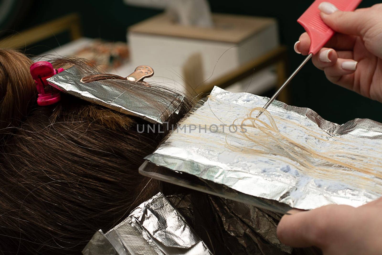 Beauty sphere. Highlighting. Air touch. Hair coloring in a beauty salon. A master hairdresser-colorist dyes a client's brown hair blond. Apply lightening powder to hair on foil with a brush. Close-up.