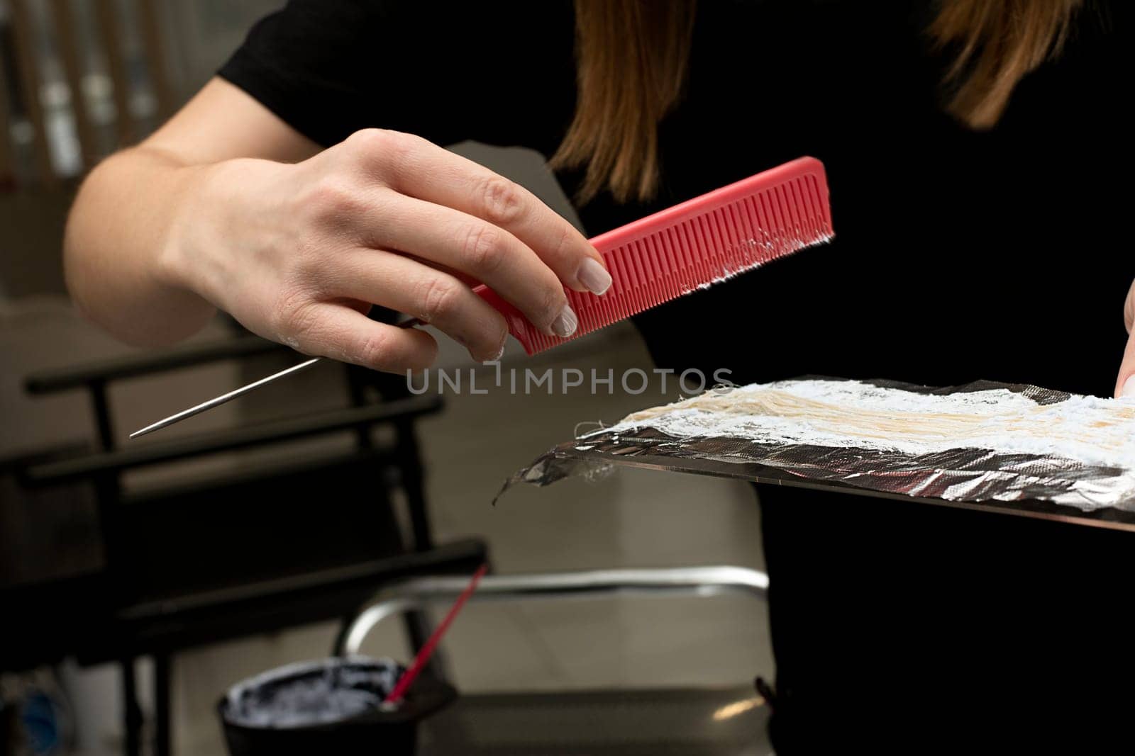 Beauty sphere. Highlighting. Air touch. Hair coloring in a beauty salon. A master hairdresser-colorist dyes a client's brown hair blond. Apply lightening powder to hair on foil with a brush. by ketlit