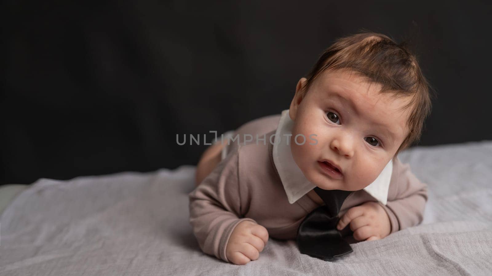 Portrait of a baby lying on his stomach wearing a tie on a black background