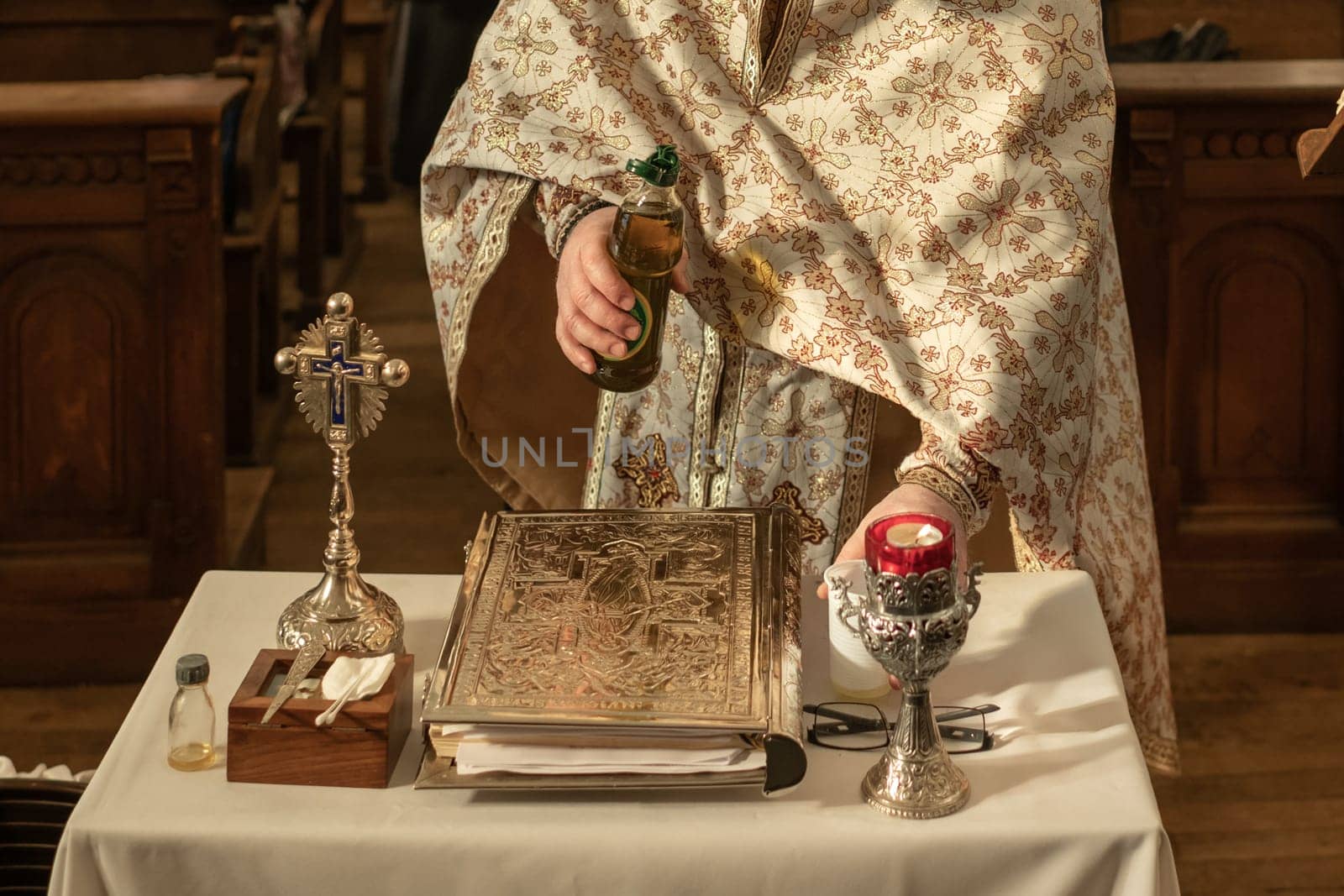 A priest in a cassock prepares oil for a child's baptism