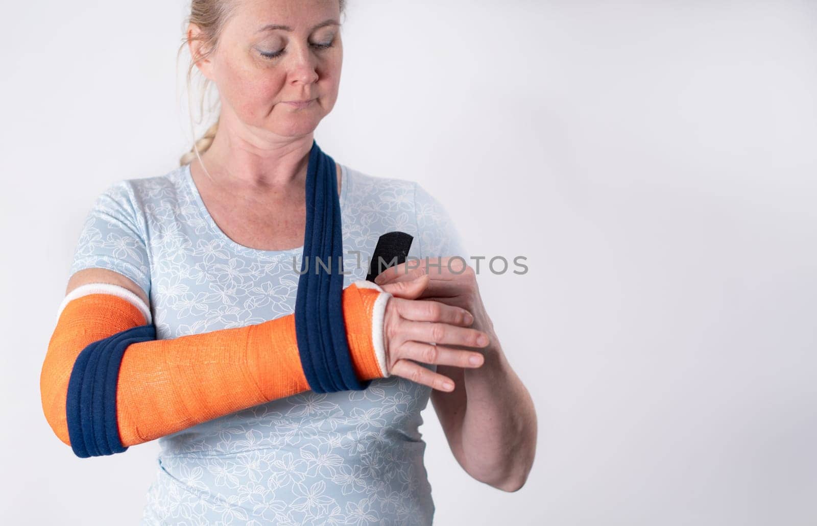 middle aged woman with broken arm in cast hangs her arm in a sling, modern treatment methods, on a neutral background by KaterinaDalemans