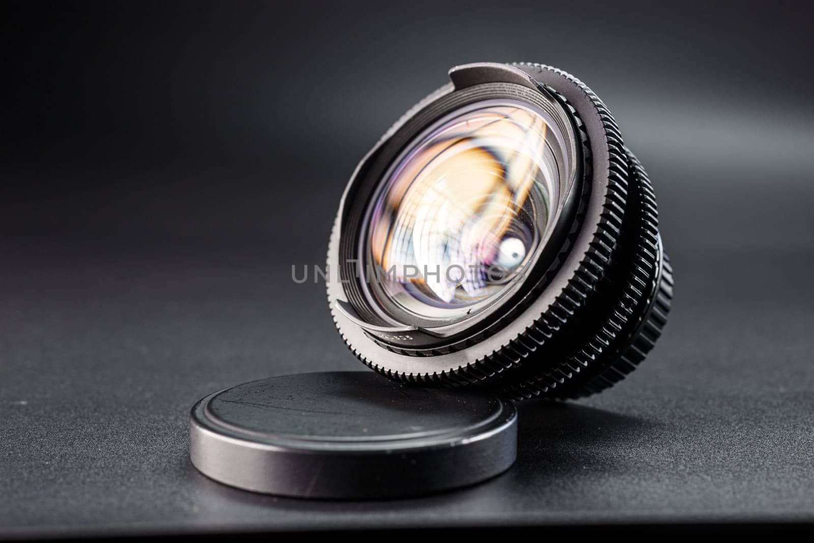 Artistic view of a vintage lens with vibrant reflections, focus on detailed ring textures, essential photography equipment on dark surface with lens cap