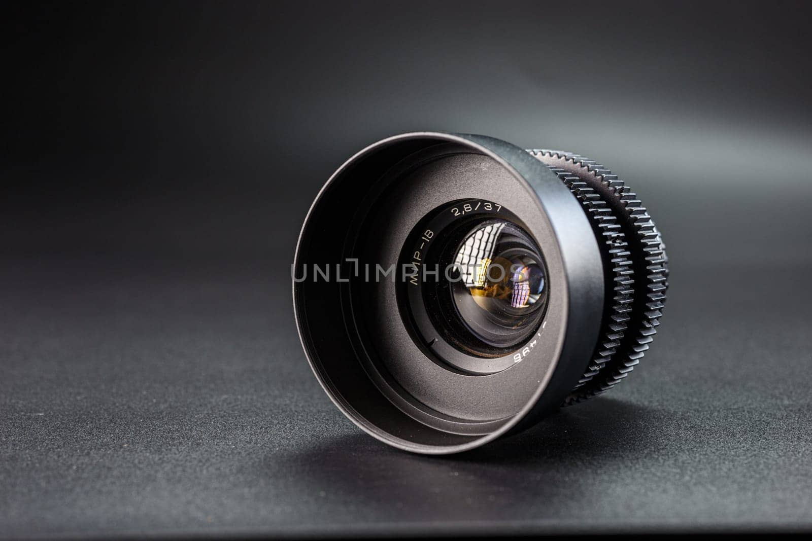Slanted black camera lens capturing clear reflections, marked with 2.8 37 , premium photography equipment against a dark, soft-focus background by mosfet_ua