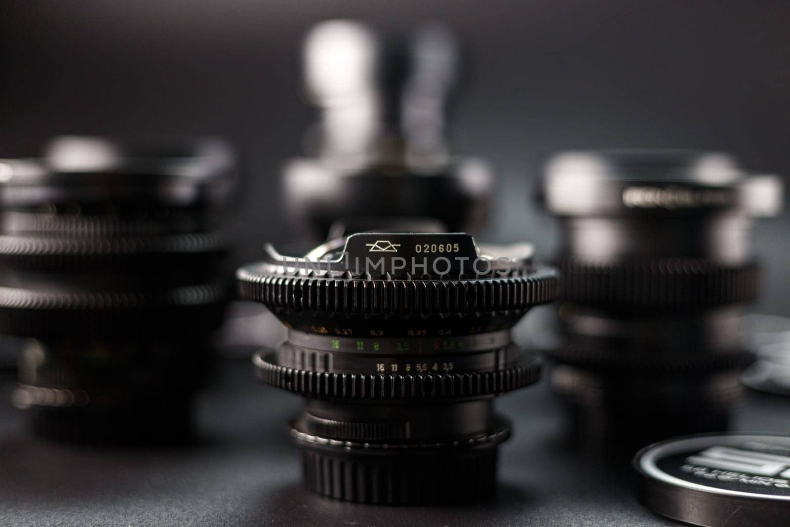 Selective focus on a vintage camera lens with serial number, surrounded by blur of other lenses, photography equipment array, black background setting by mosfet_ua