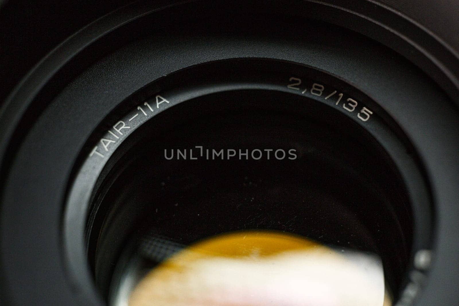 Detailed view of TAIR-11A camera lens engraving, with focal length and aperture value, precision instrument for photography, against a blurred dark background.