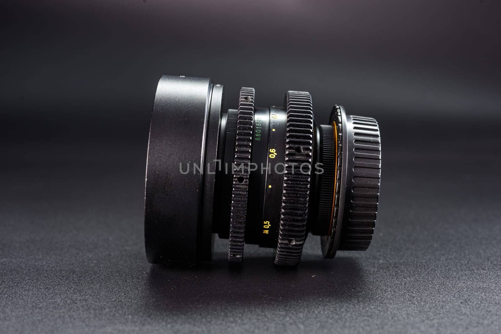 Side angle of antique camera lens showcasing focus dials, numbered settings, photography enthusiasts collectible, placed against gradient dark background by mosfet_ua