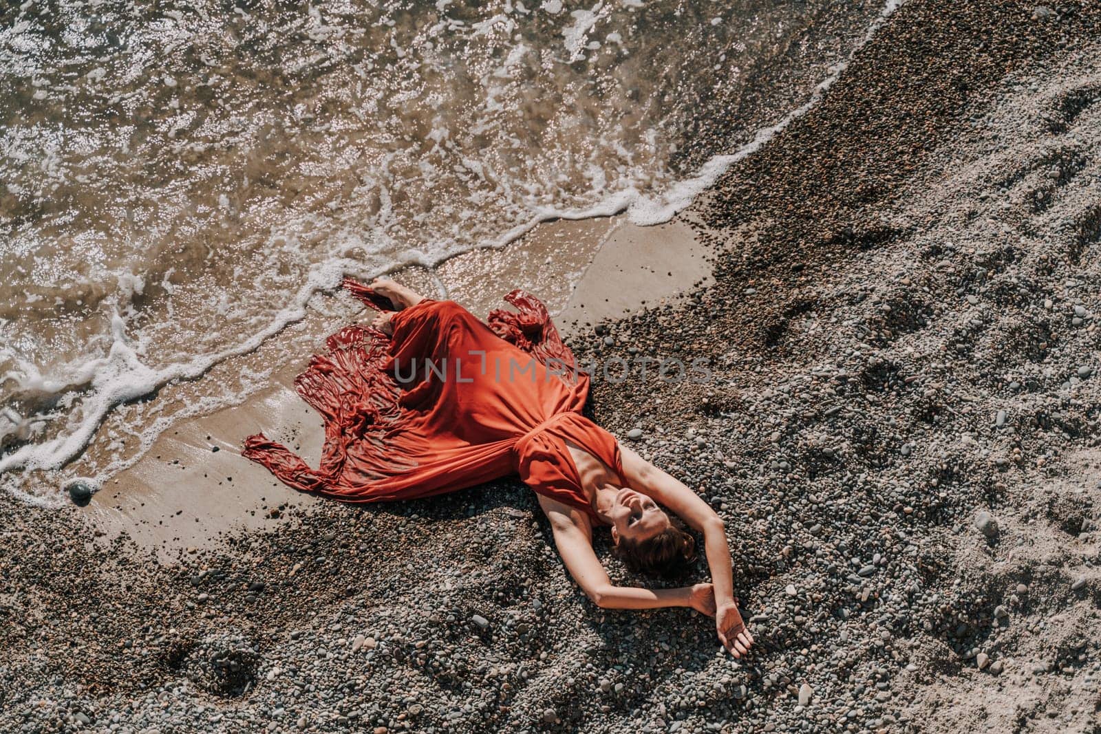 Woman red dress sea. Female dancer in a long red dress posing on a beach with rocks on sunny day by Matiunina