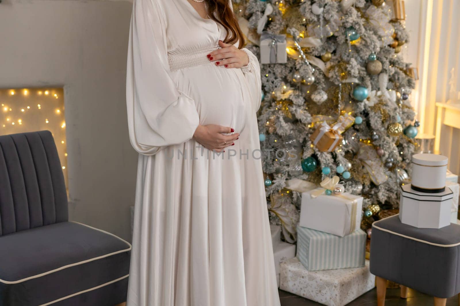 Pregnant woman holding a belly against Christmas tree with lights. family holiday concept