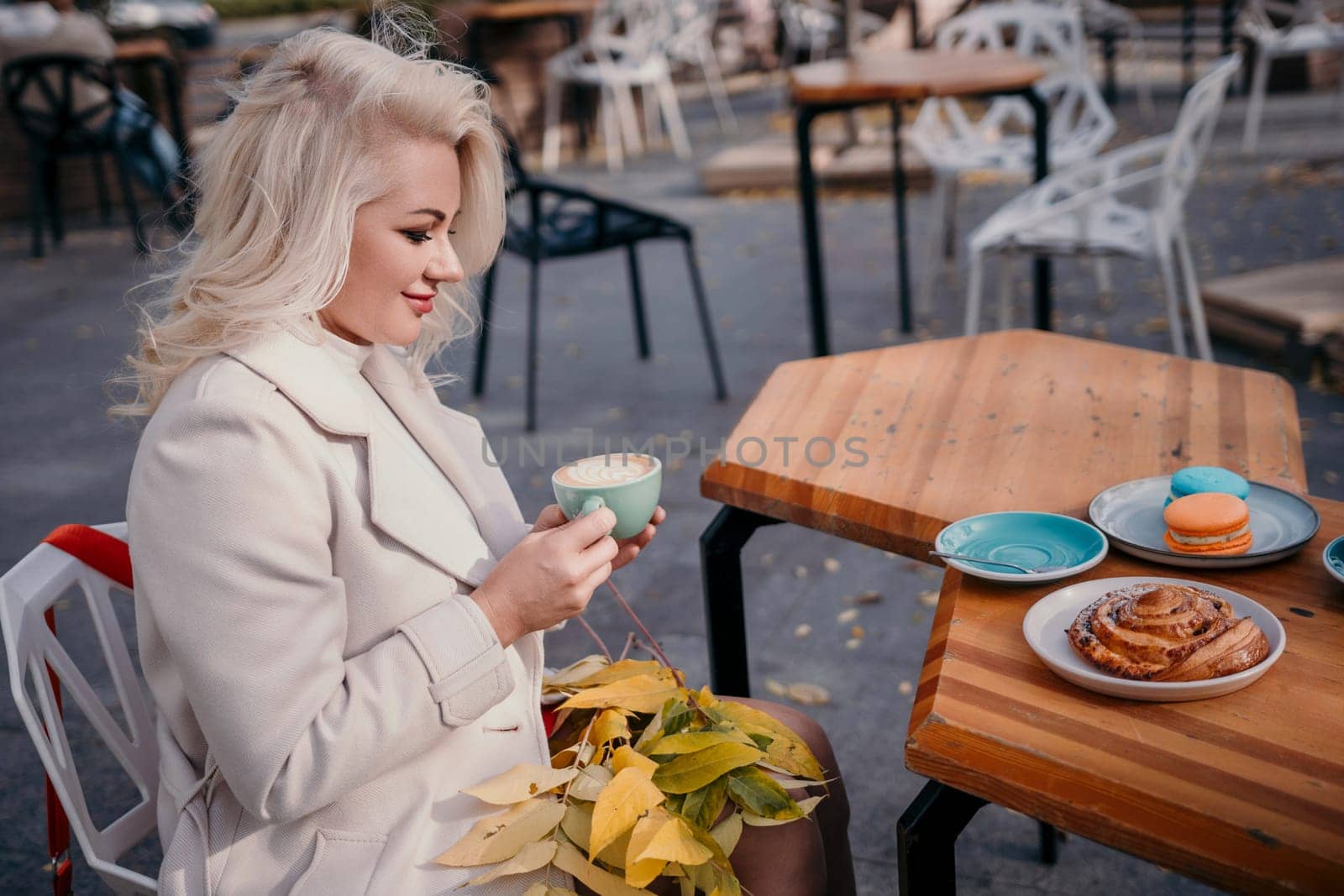 A woman is sitting at a table with a pastry and a cup of coffee. She is wearing a white coat and has blonde hair