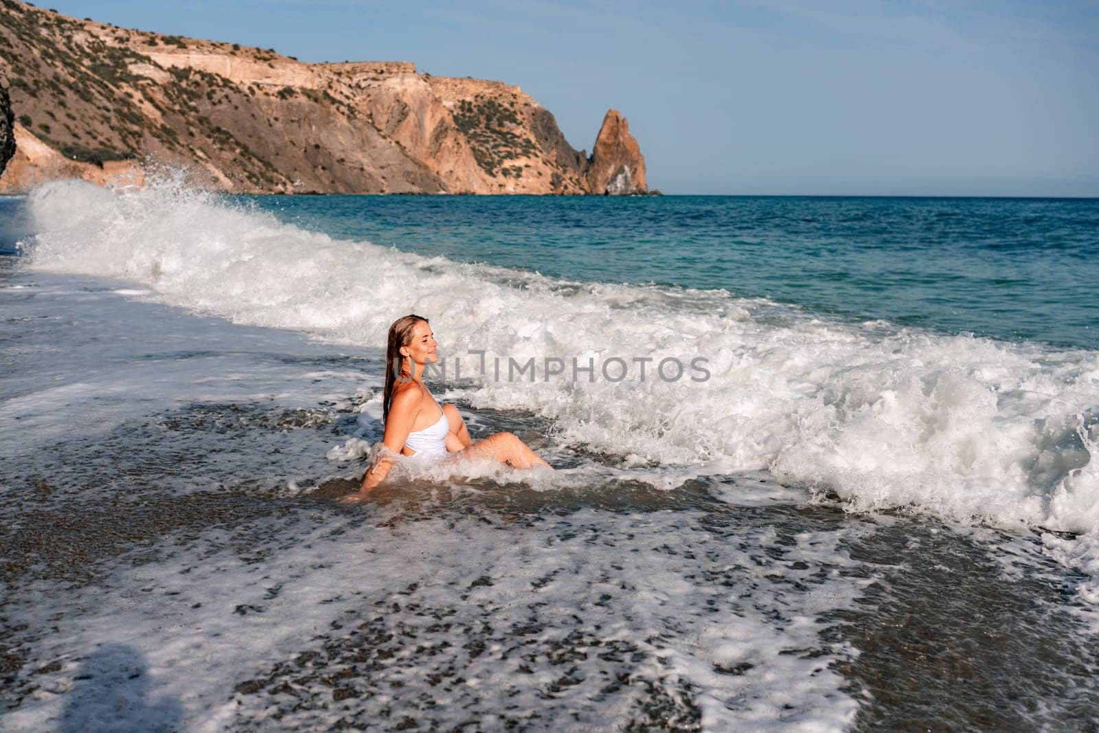 Happy woman in bikini sits on the sea beach. Tanned girl sunbathing on a beautiful shore. Summer vacation or holiday travel concept by Matiunina