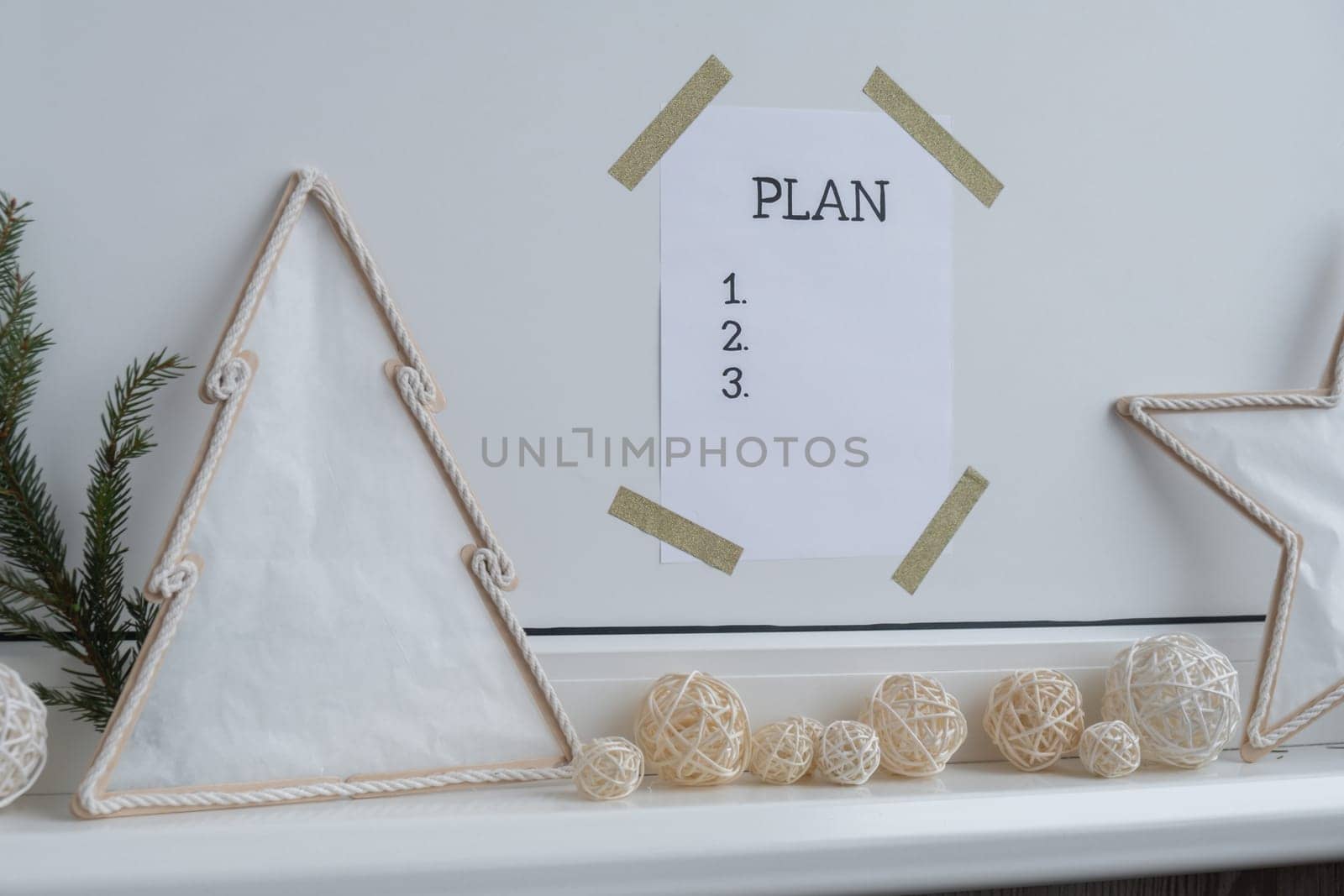 PLAN checklist text on paper note stick on while wall with cozy minimalistic handmade Christmas decor. New year aims resolutions. Low key festive Planning and setting goals concept