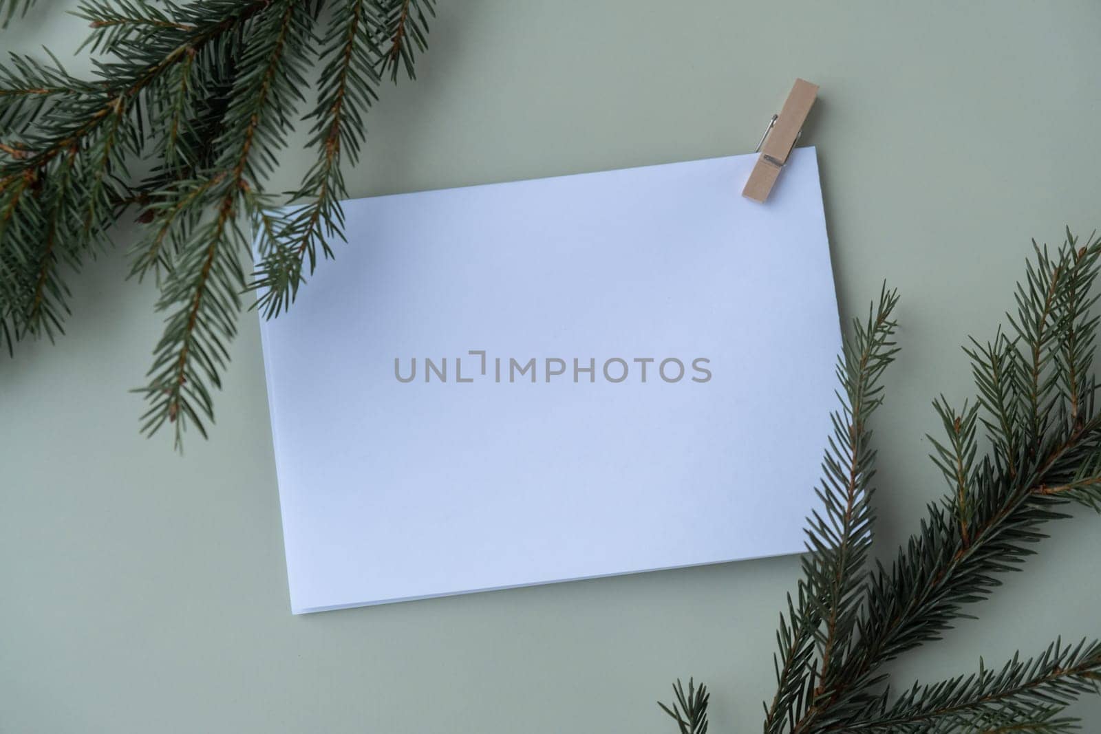 Green background with Christmas tree branch decor and copy space mock up white envelope. Template for Christmas greeting card New Year postcard. Flat lay by anna_stasiia