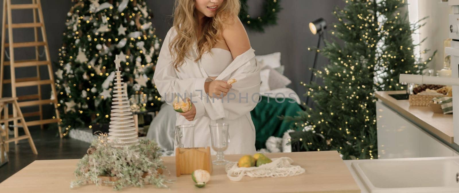 Woman Kitchen Christmas decor in white shirt, peeling tangerines. Illustrating New Year's mood holiday preparations.