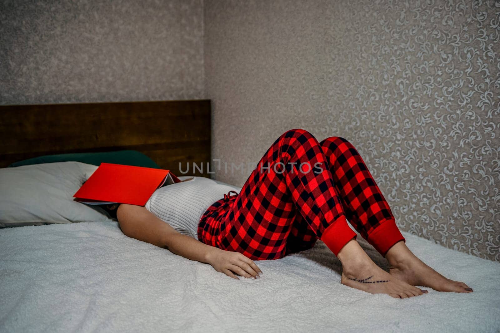 Balancing work, studies, and reading at home: Woman in red checkered pants lying on her bed with a red book and notes . by panophotograph