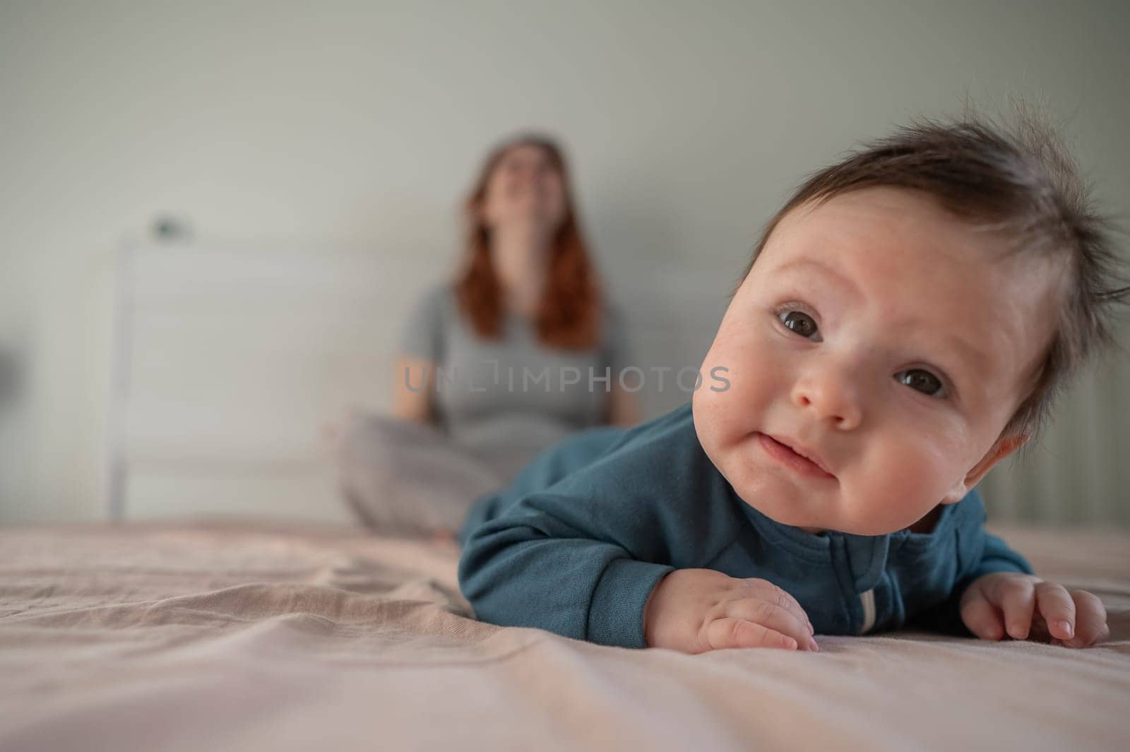 A three-month-old boy lies on his stomach on the bed and his mother sits behind him and cries. Postpartum depression. by mrwed54