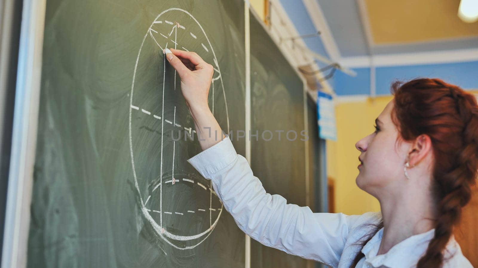 A red-haired schoolgirl draws geometric shapes on the board
