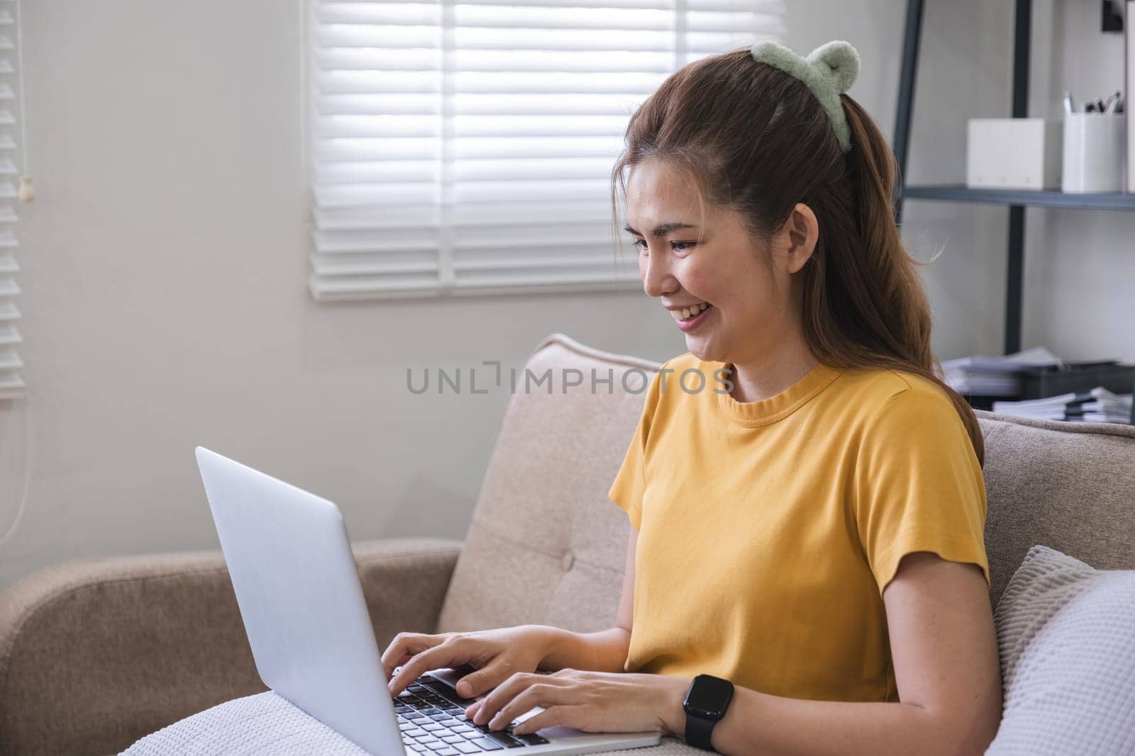 A woman is sitting on a couch with a laptop in front of her.