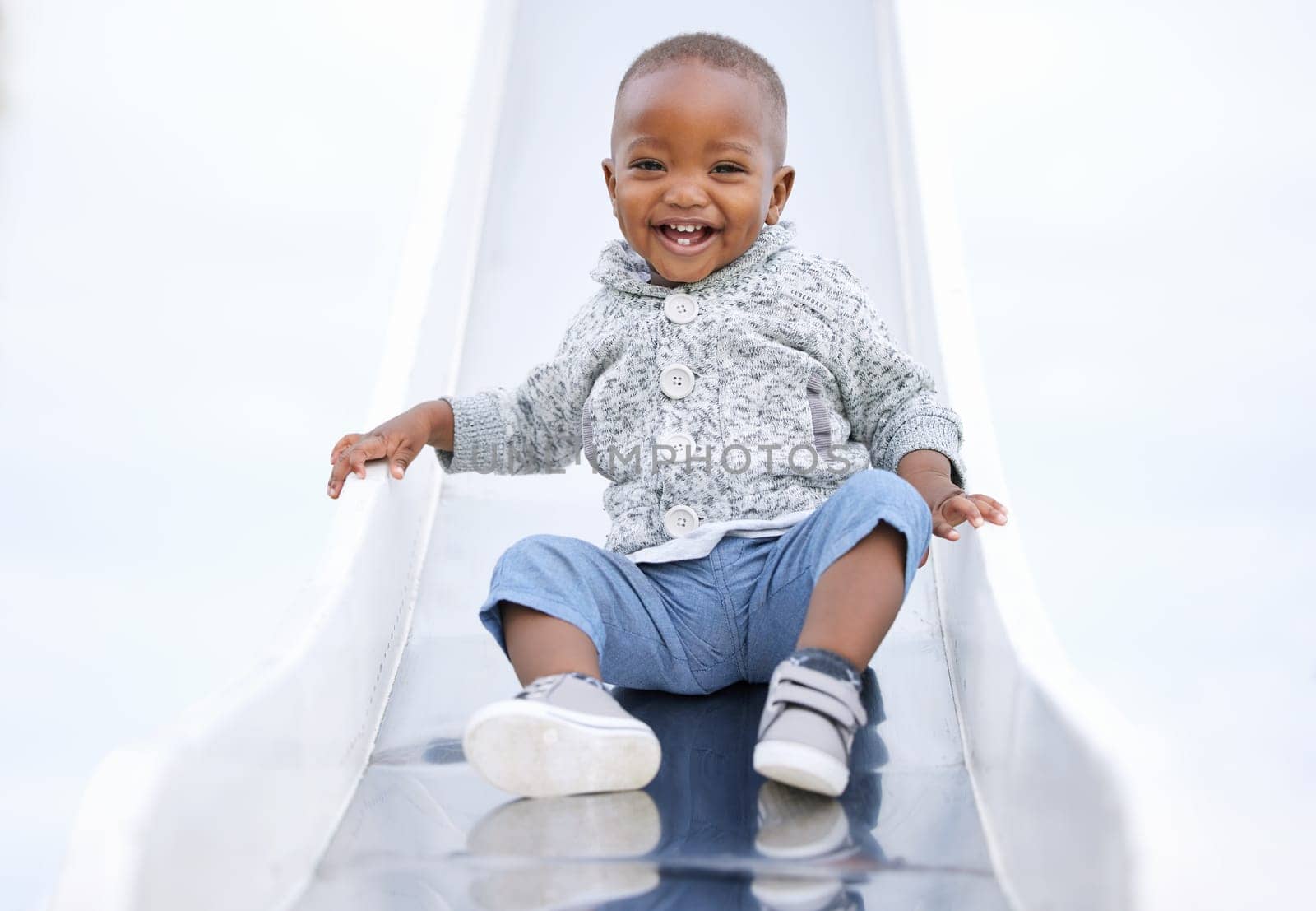 African baby, boy and slide at playground, portrait and excited for playing, learning and play in summer. Toddler, child and happy at park for games, laugh or outdoor for development at kindergarten.