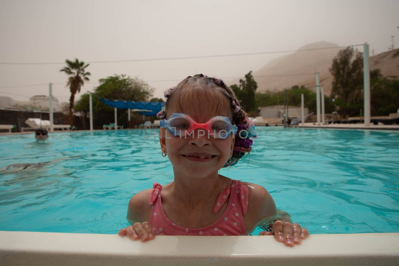 A girl with glasses and bright pigtails swims in the pool by gordiza
