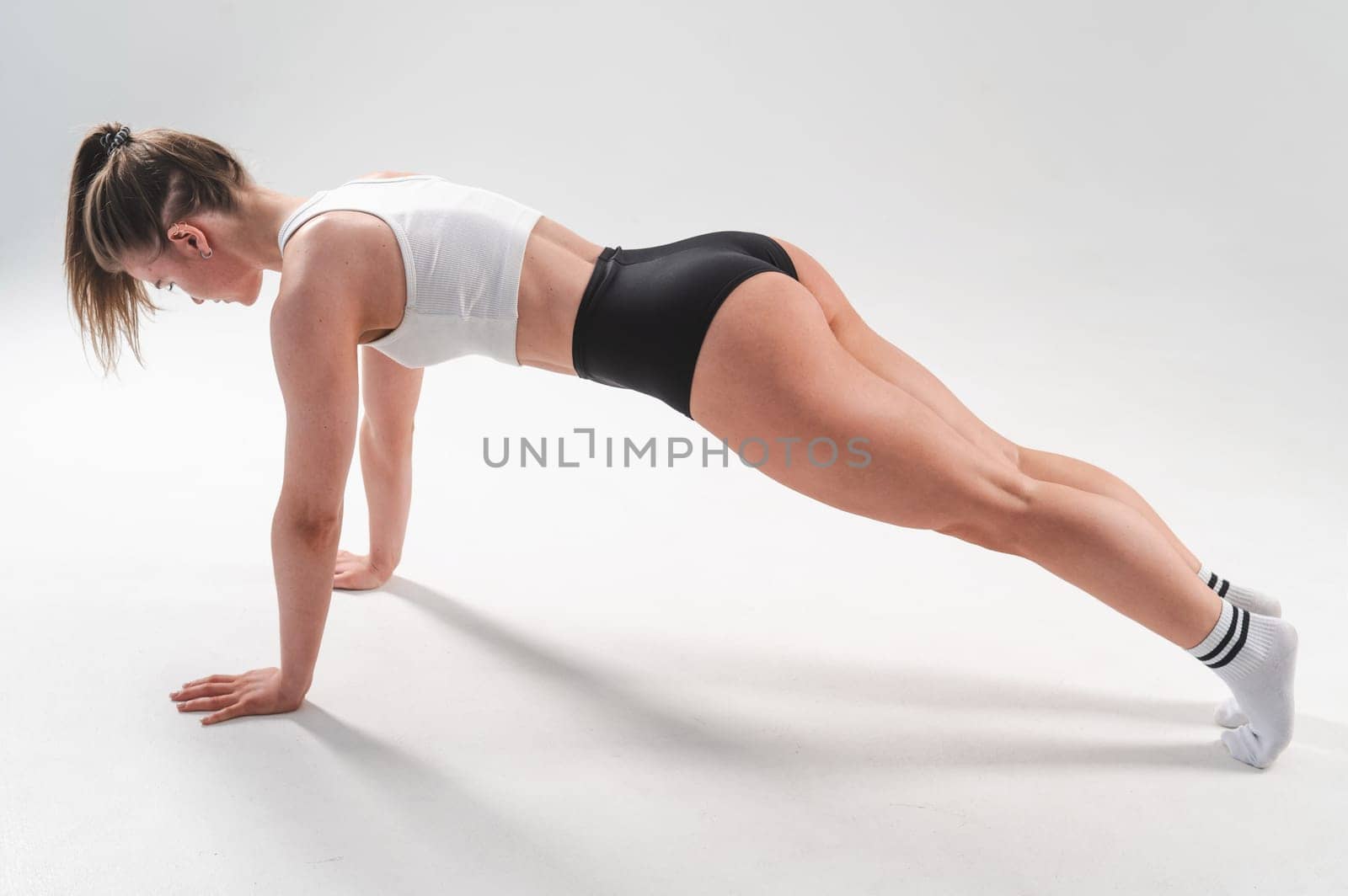 Athletic woman in shorts doing plank on white background