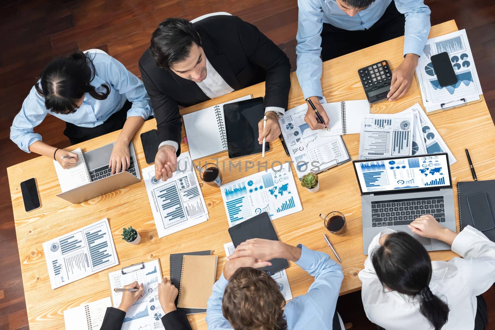 Wide top view of diverse group of business analyst team analyzing financial data report paper on meeting table. Chart and graph dashboard by business intelligence analysis. Meticulous