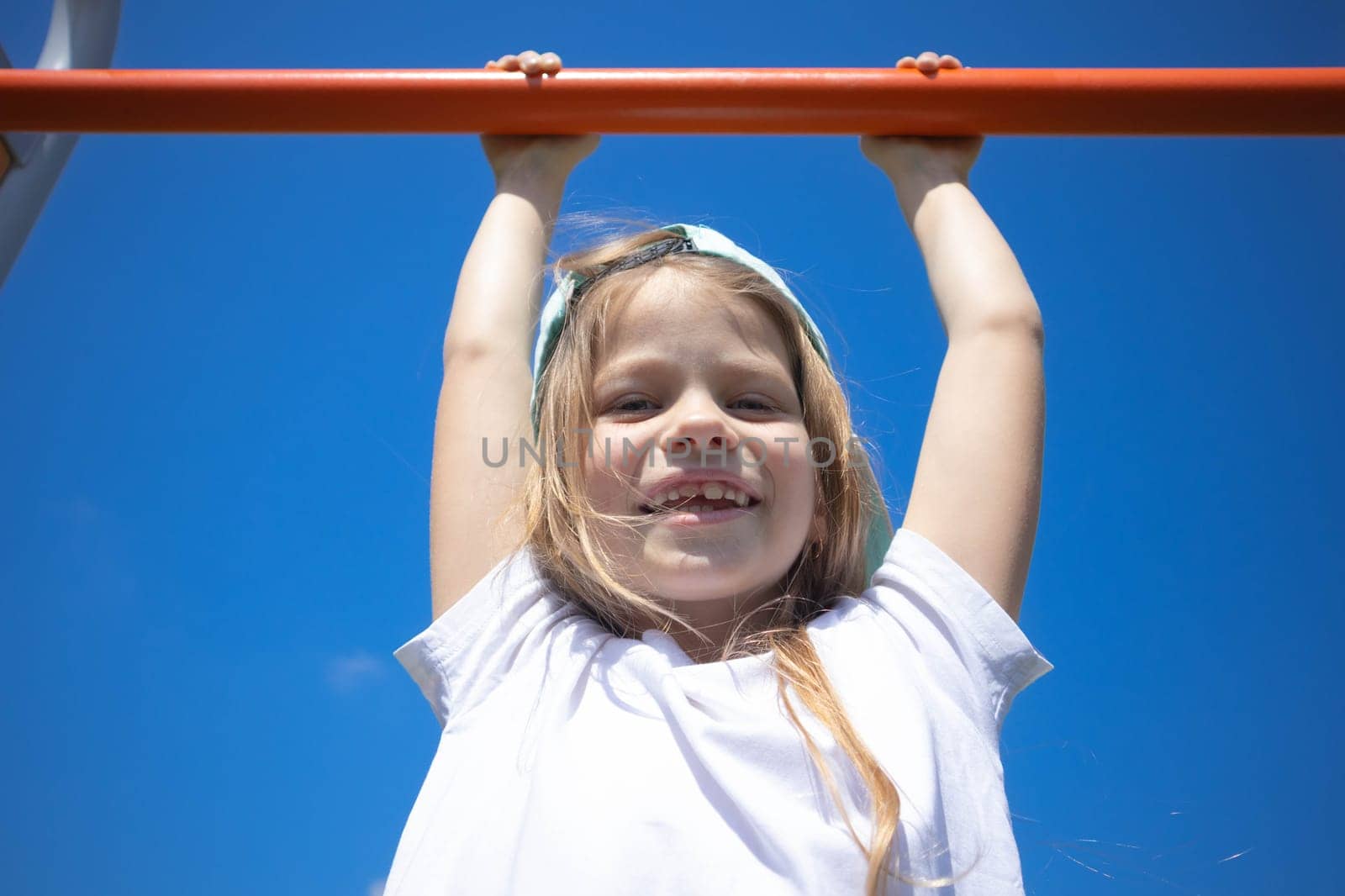 A girl hangs on a horizontal bar against a blue sky. High quality photo