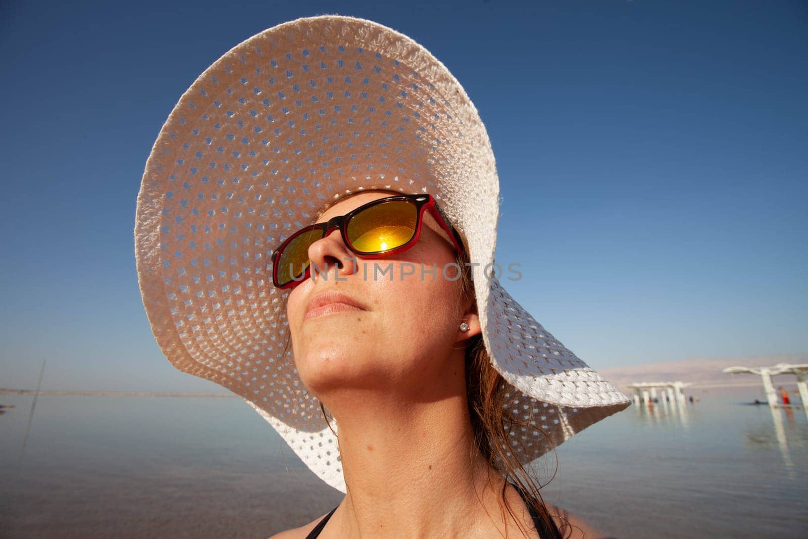 A girl in sunglasses basks in the sun against the background of the Dead Sea by gordiza