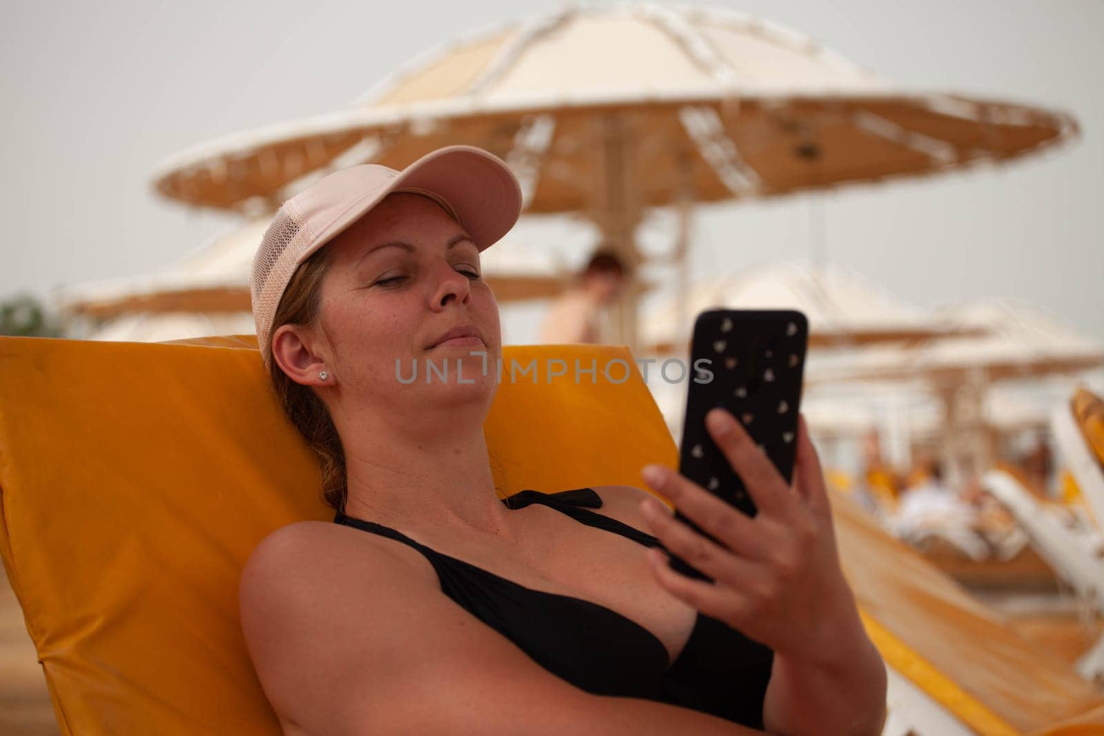 Girl looking at the phone on the beach by gordiza