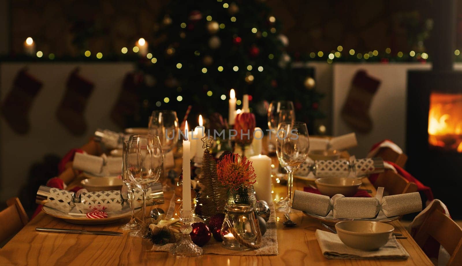 Dinner, table and Christmas in home with candles at night, love and celebration for holidays. Feast, dining and house or dark with lights for xmas, flowers and bowls or wine glasses at fireplace.