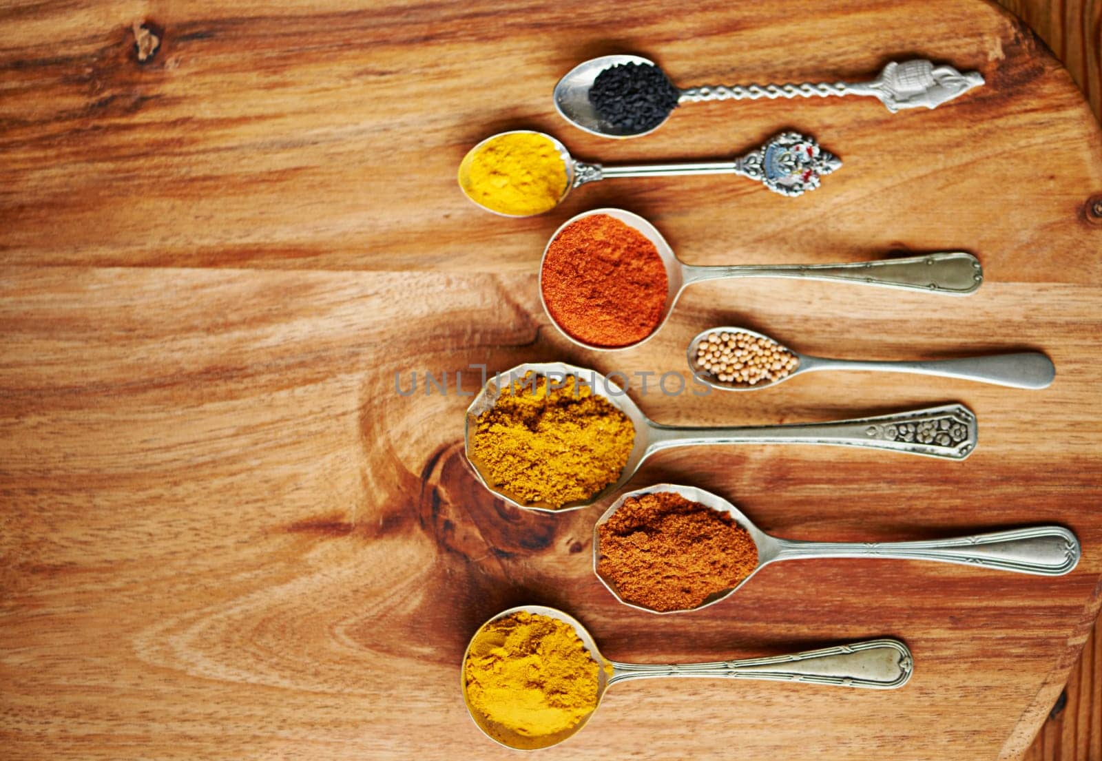 Spoons, spice and selection of ingredients for seasoning on kitchen table, turmeric and paprika for meal. Top view, condiments and options for cooking in Indian culture, cumin and food preparation.