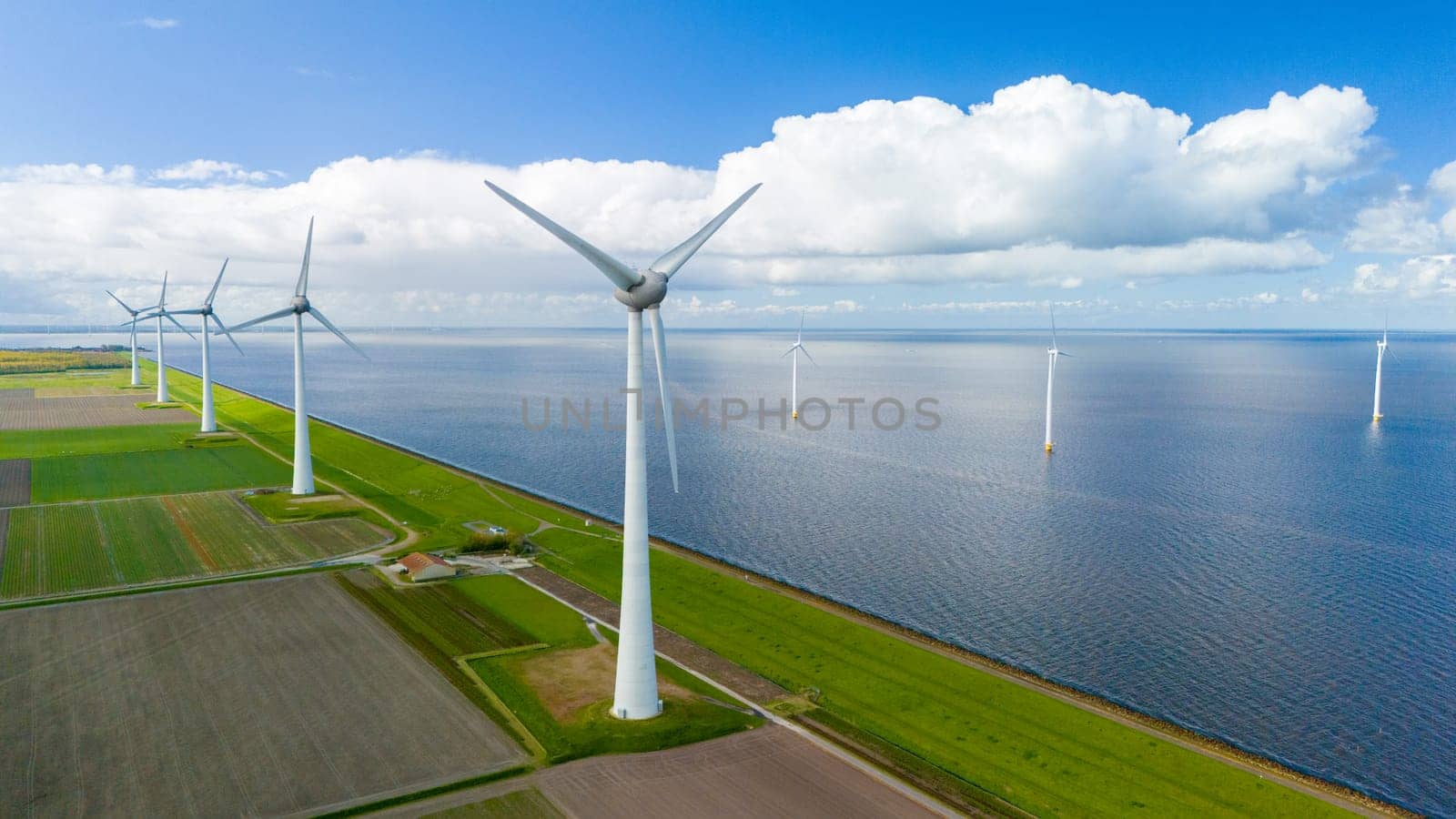 Wind turbines spin gracefully in a wind farm perched near the ocean, harnessing the power of the breeze to generate renewable energy. in the Noordoostpolder Netherlands