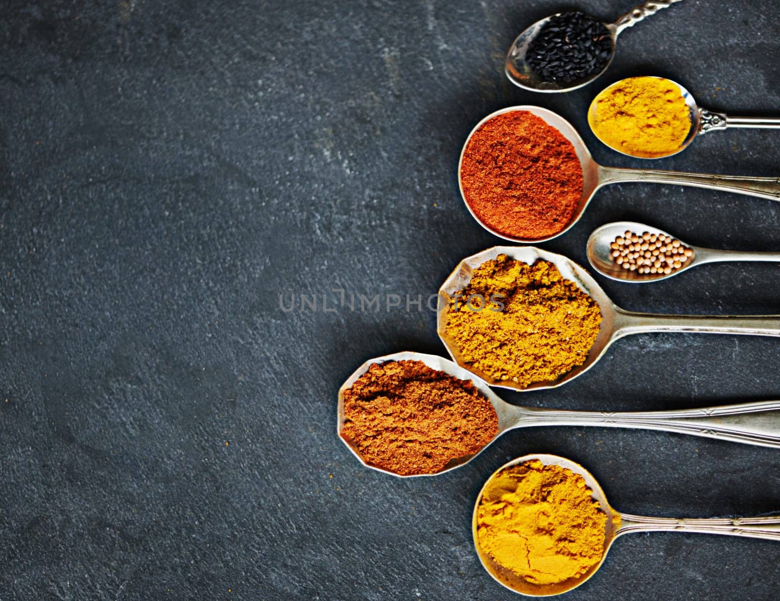 Spoon, powder and group of spices by dark background for cooking dinner, health and nutrition. Turmeric, chilli and seeds on black surface with zoom for Oriental food, antioxidant and spicy cuisine.