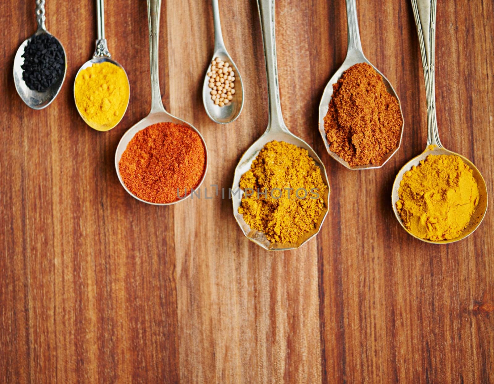 Spoons, spice and selection of flavor for seasoning on kitchen table, turmeric and paprika for meal. Top view, condiments and options for spicy cooking in Indian culture, cumin and food preparation by YuriArcurs