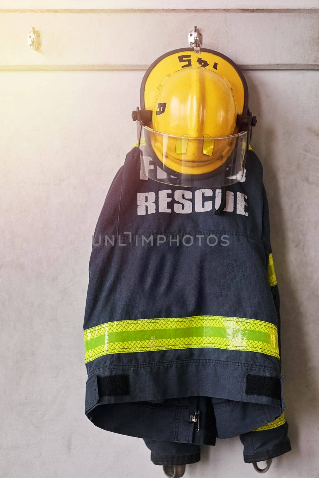 Clothing, firefighter and wall with helmet on rack for emergency services, rescue or safety at station. Closeup of fire brigade gear hanging for protection, outfit or health and security department by YuriArcurs