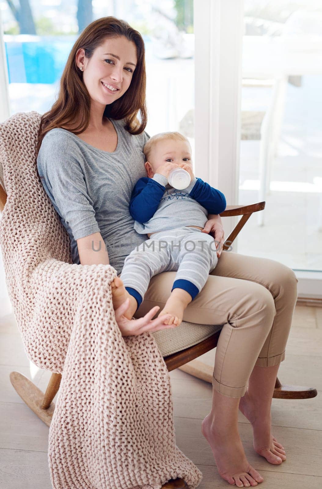 Mom, baby and smile in chair for support, love and cute as toddler for growth and child development. Woman, kid and happy at home with bottle for bonding, childhood memories and fun in portrait.