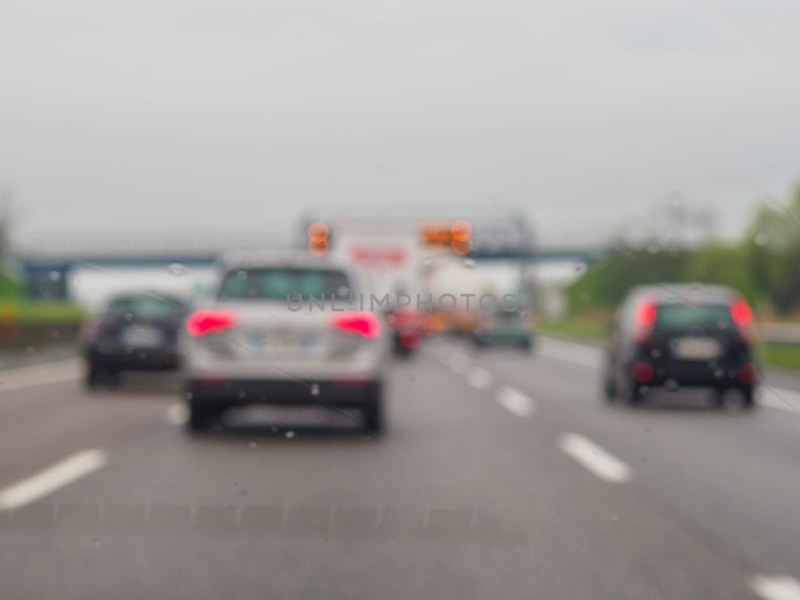 A blurry image of a busy street with cars and a truck. The rain is making the windshield of the cars and truck wet