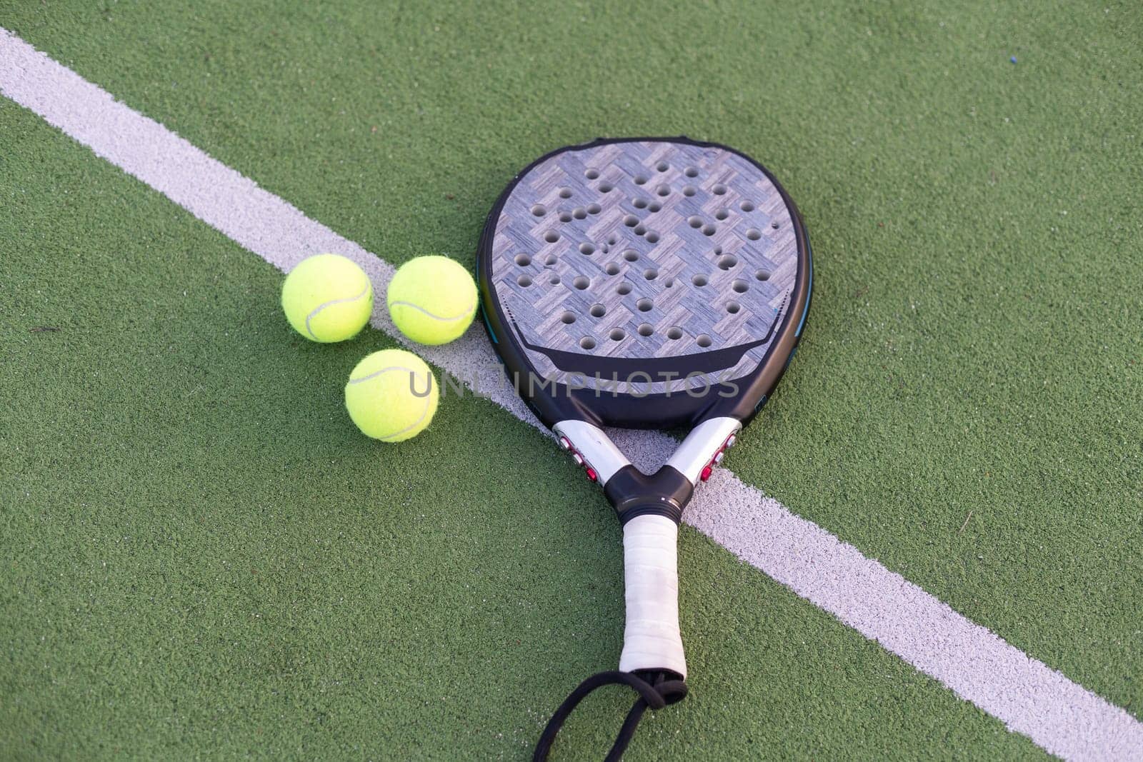 Yellow balls on grass turf near padel tennis racket behind net in green court outdoors with natural lighting. Paddle is a racquet game. Professional sport concept with copy space. High quality photo