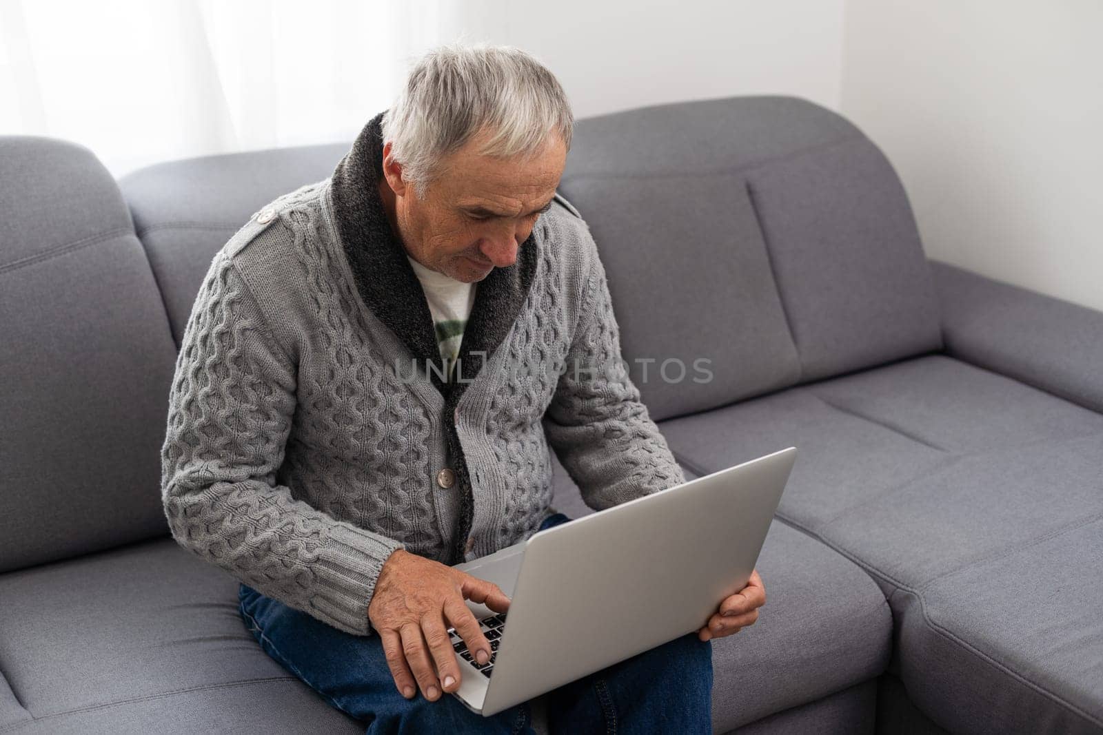 Older man sitting on sofa, smiling at computer screen at home. High quality photo