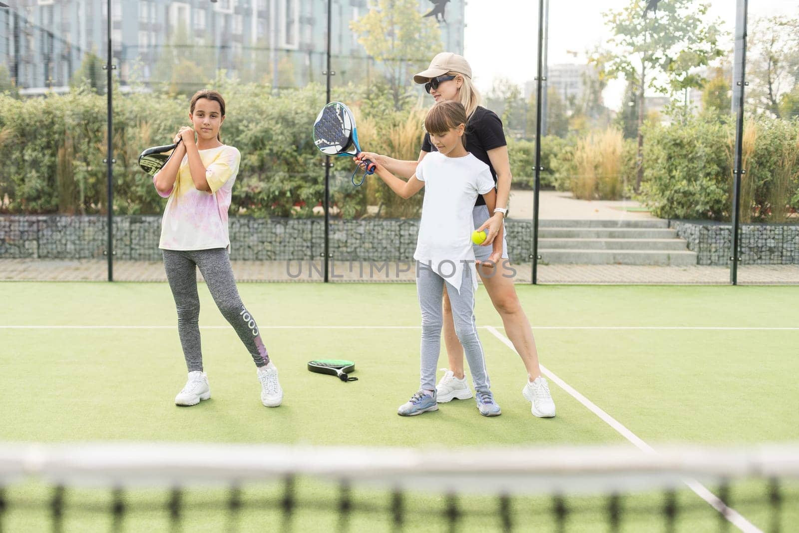 Young sporty woman with children playing padel game in court on sunny day. High quality photo