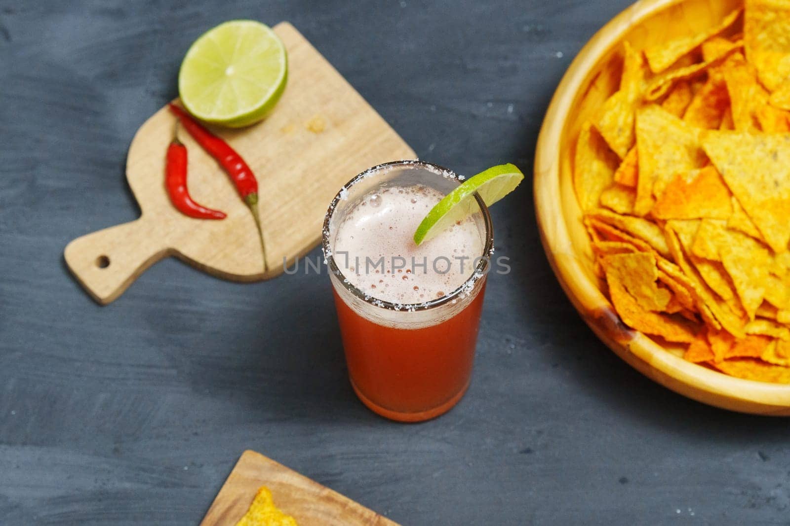 Michelada cocktail with tomato juice, beer and lime in a glass and nachos. Selective focus by darksoul72