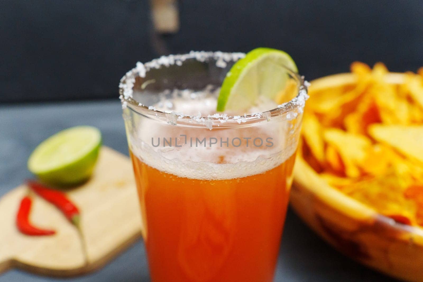 Michelada cocktail with tomato juice, beer and lime in a glass and nachos. Selective focus