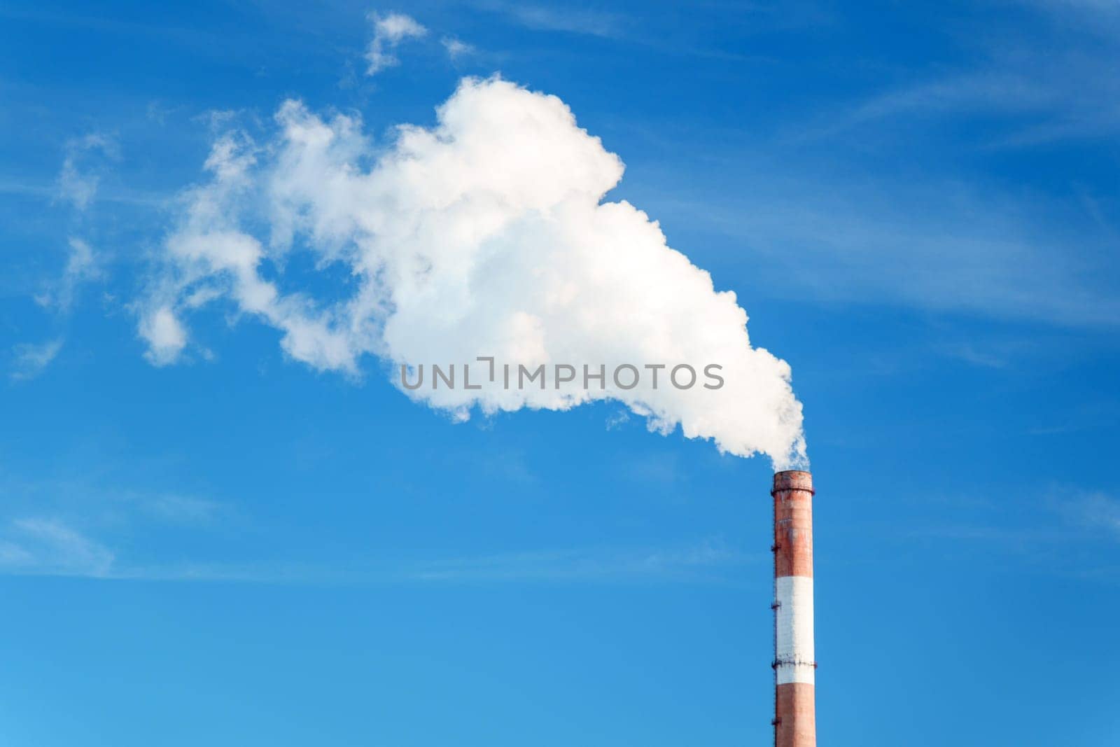 Smokestack emits thick smoke from a pipe, contrasting against a clear blue sky