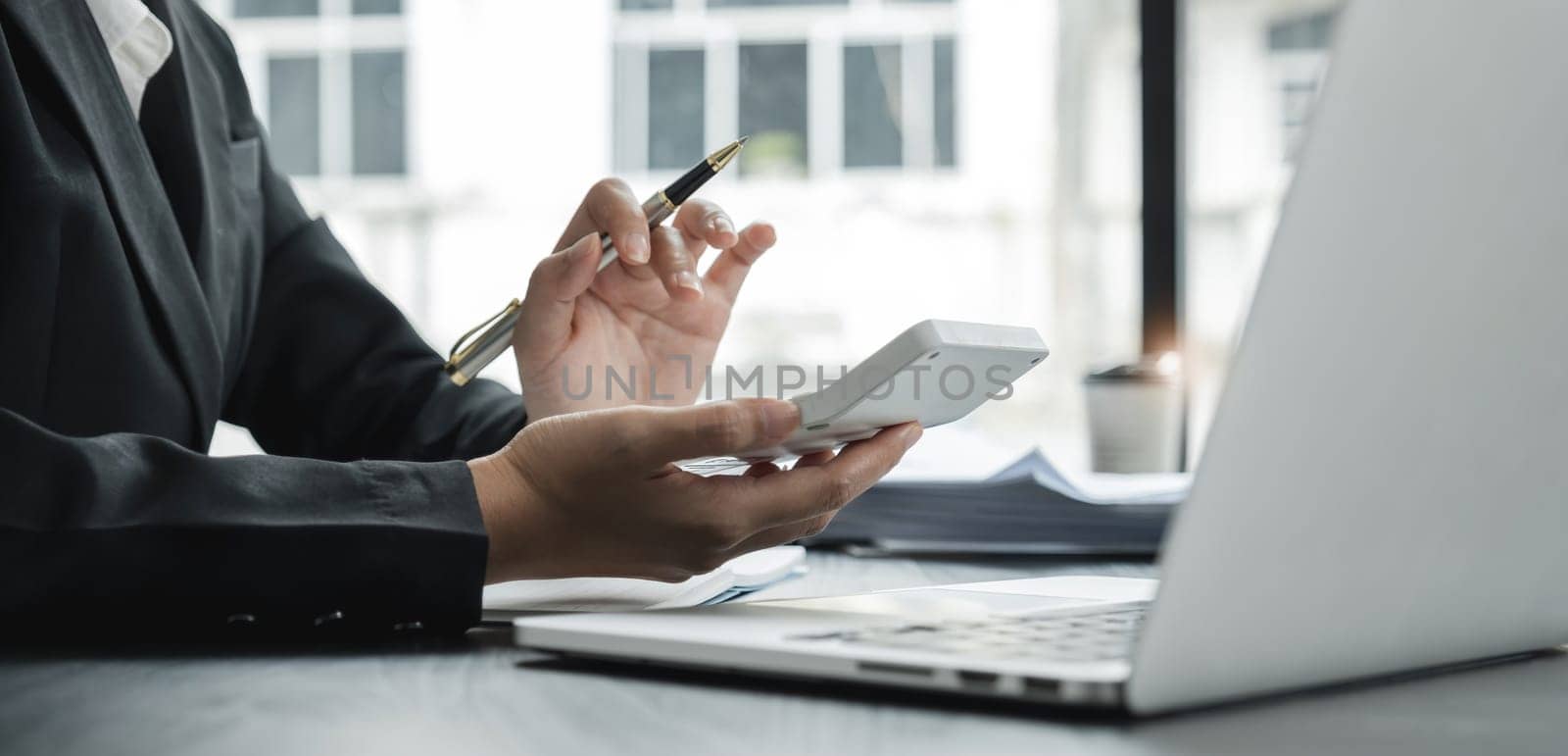 Close up Business woman using calculator and laptop for do math finance on wooden desk in office and business working background, tax, accounting, statistics and analytic research concept.
