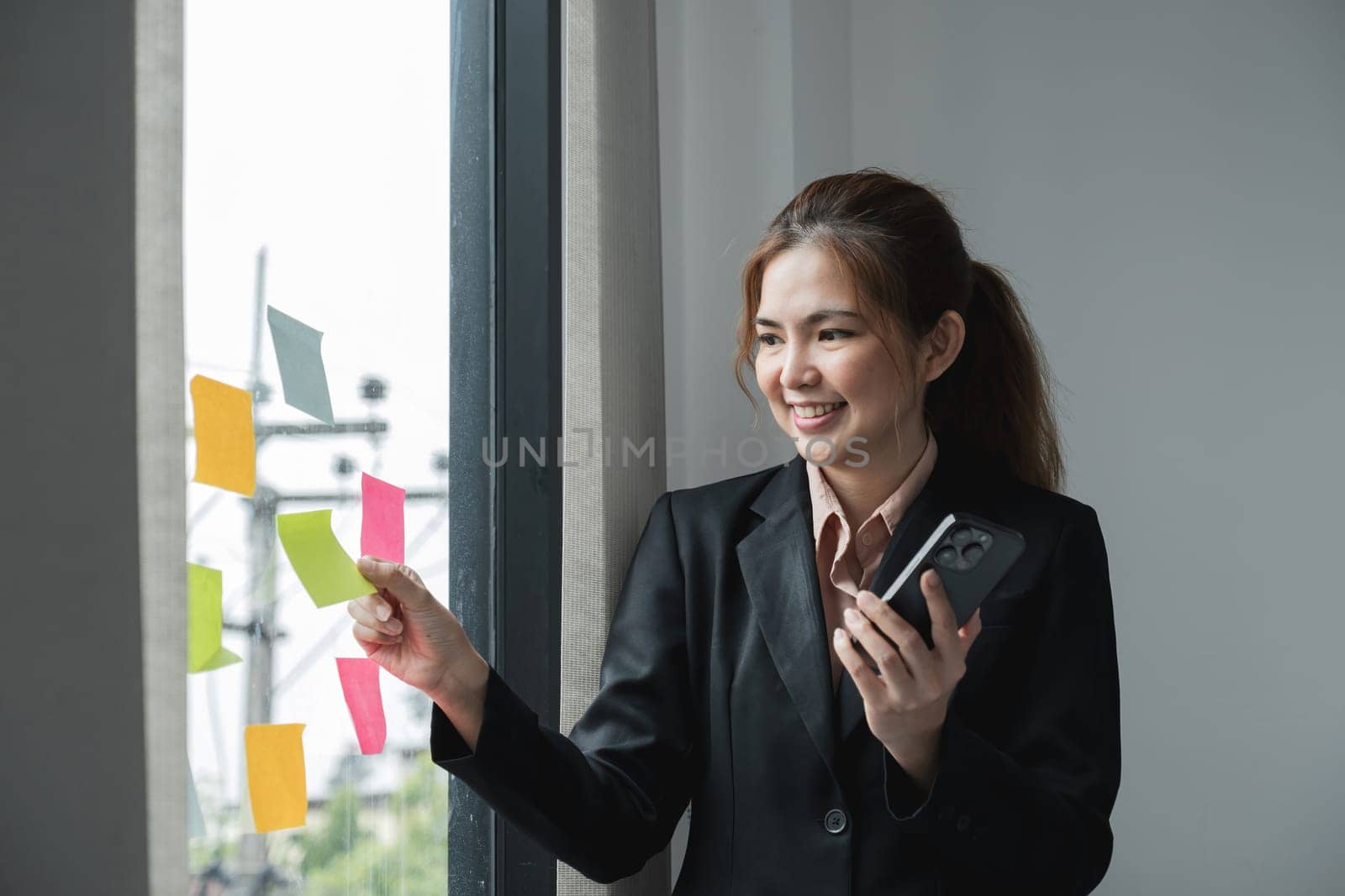 Young creative woman professional using sticky notes in glass wall to writing strategy business plan to development grow to success. Happy asian woman working at office. by wichayada